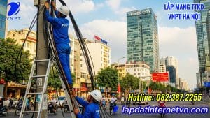 Hai nhân viên VNPT đang lắp đặt cáp quang trên cột điện tại phường Vĩnh Tuy, với khu đô thị Times City và đường phố đông đúc ở phía sau, thể hiện hạ tầng mạng vững chắc của dịch vụ Lắp mạng Internet VNPT Phường Vĩnh Tuy.